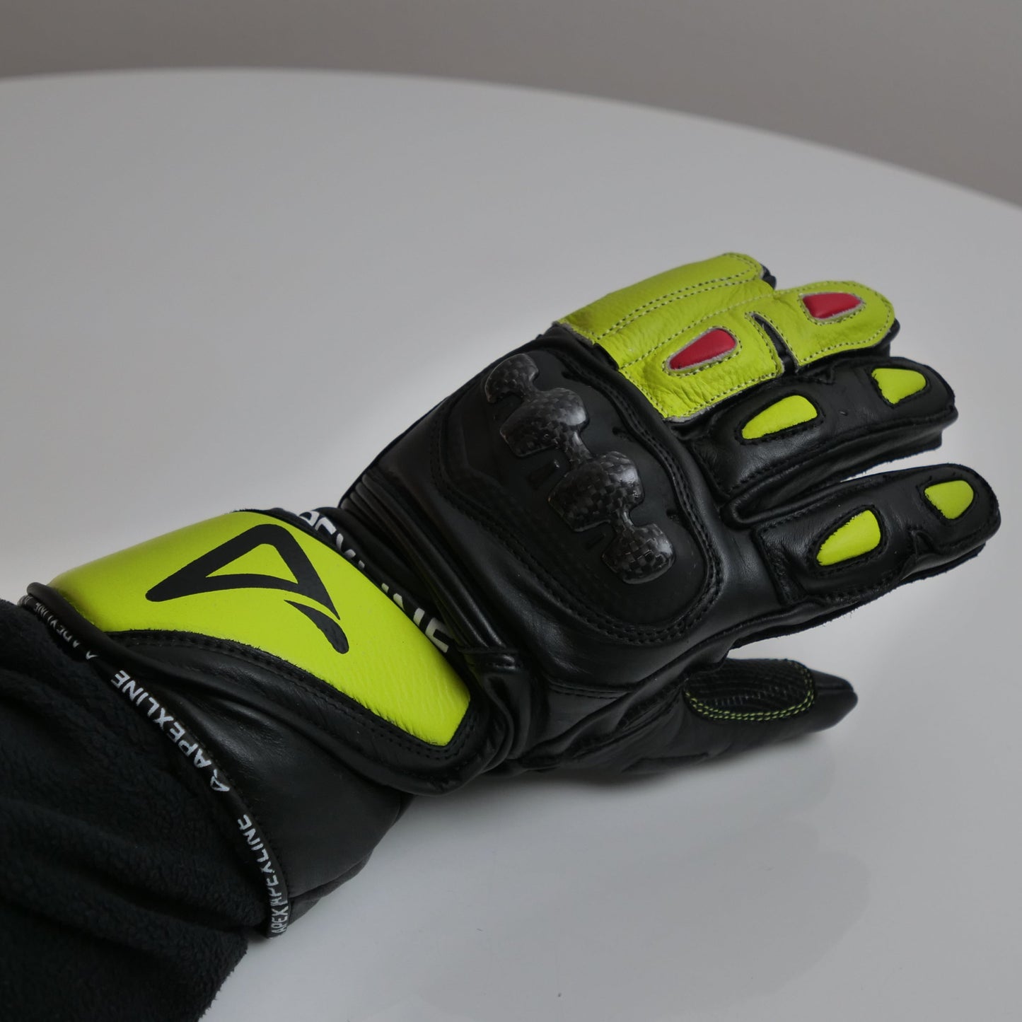 APEXLINE Motorradhandschuh auf weißem Hintergrund, Fokus auf Carbon-Knöchelprotektor und leuchtend gelbe Designelemente.